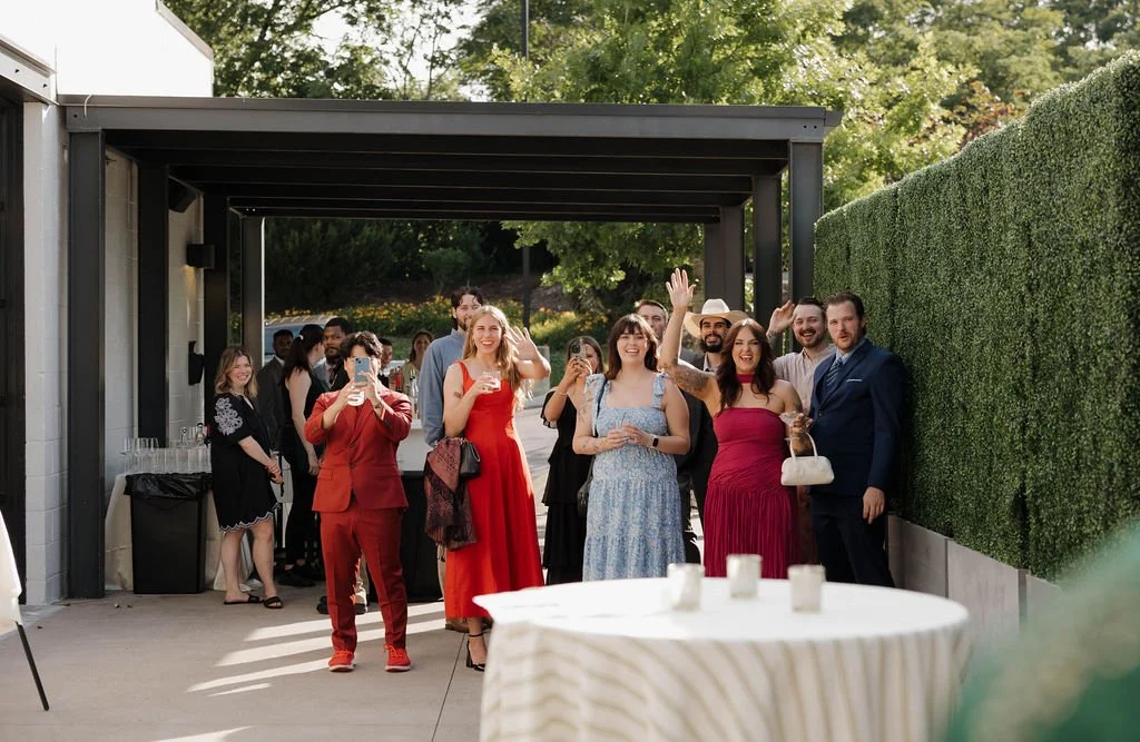 Guests cheer on the patio under a black pergola beside a boxwood hedge wall