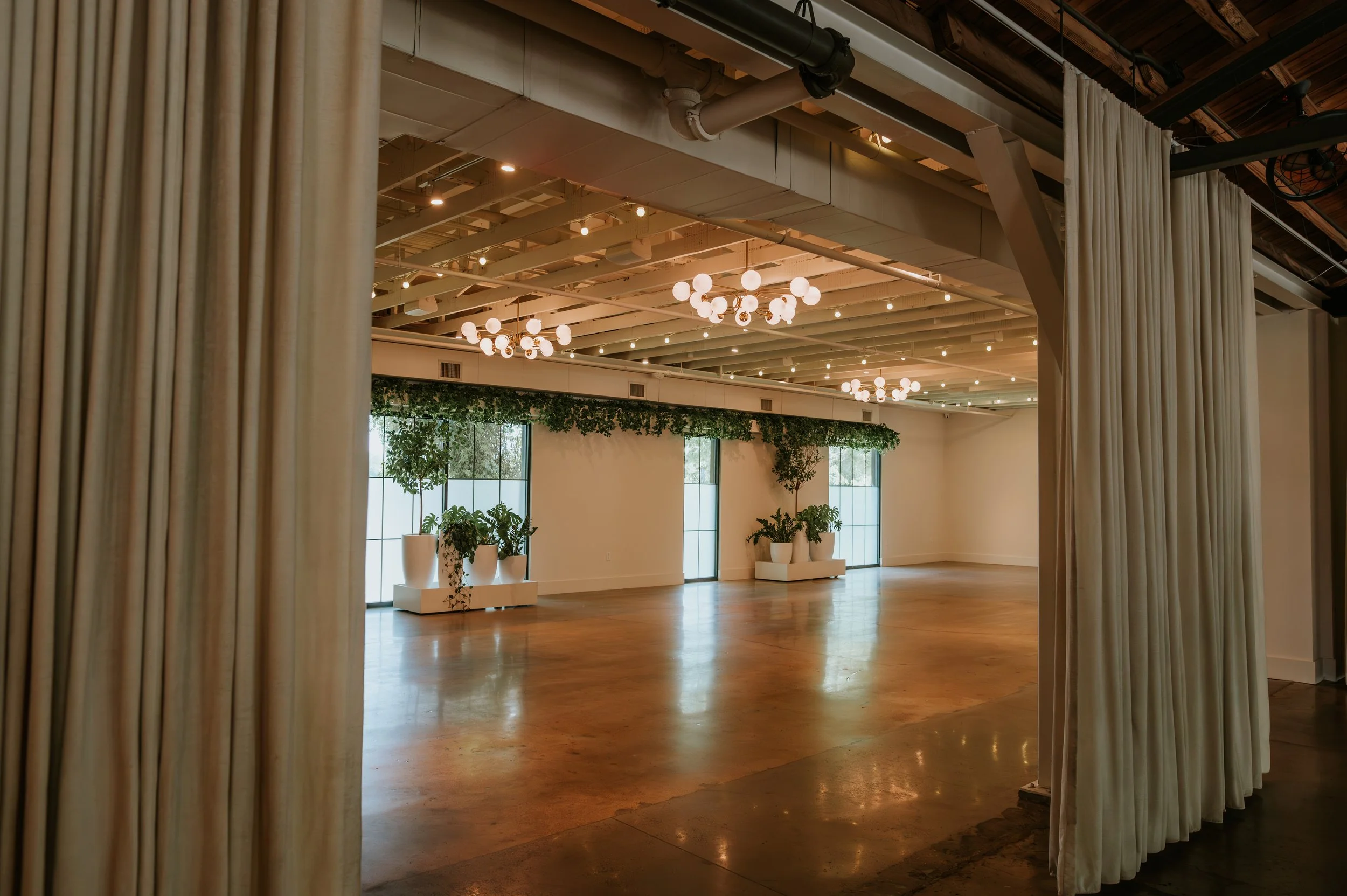 Empty Conservatory seen through open drapes, with globe chandeliers, polished concrete floors and tall windows