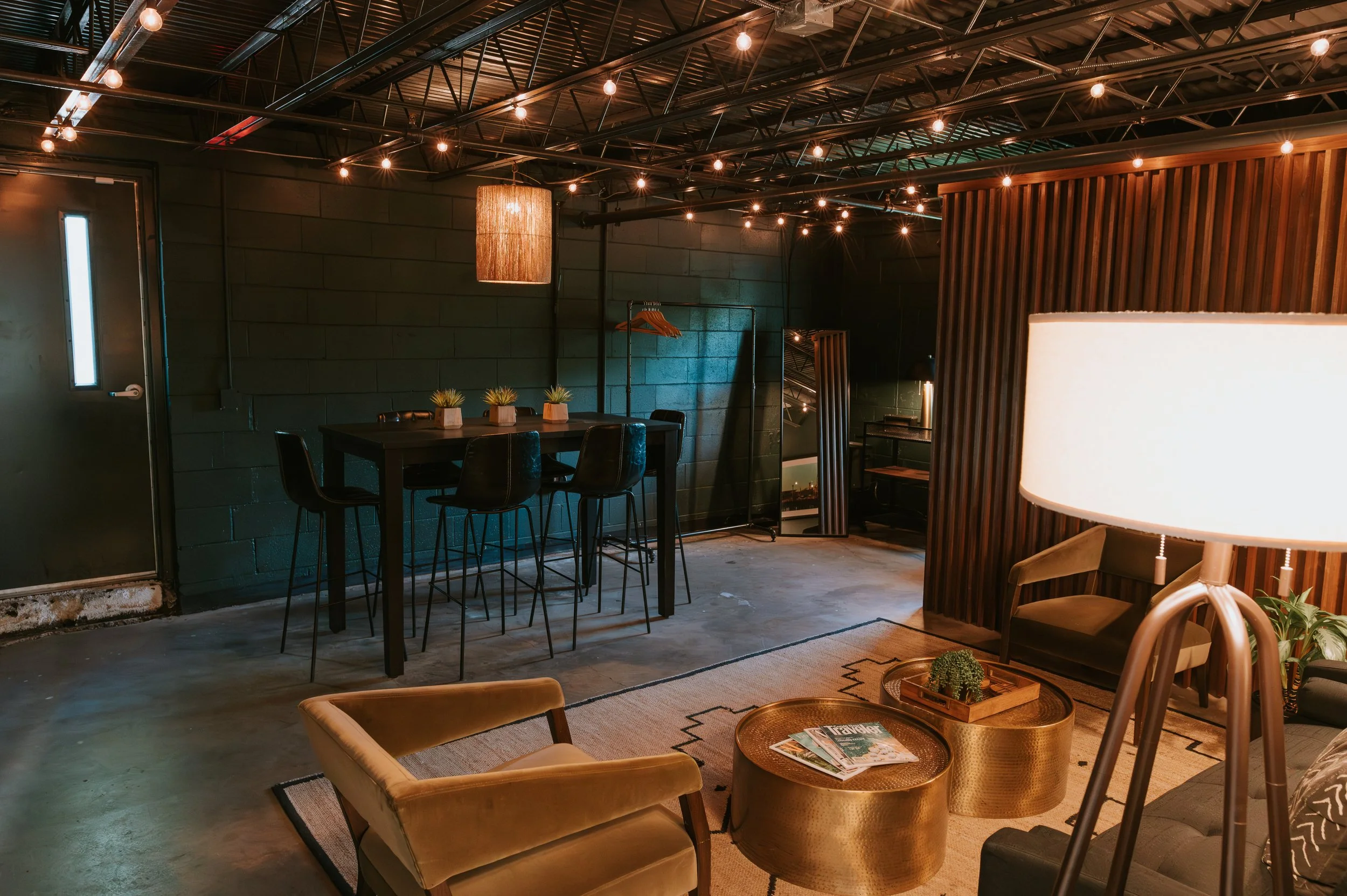 Mid-century lounge with brass drum tables, a leather chair, high-top seating and a wood-slat accent wall