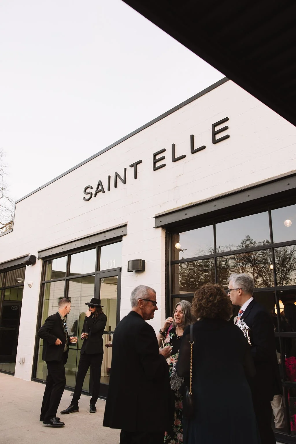 Guests in formal wear gather outside the Saint Elle entrance at dusk