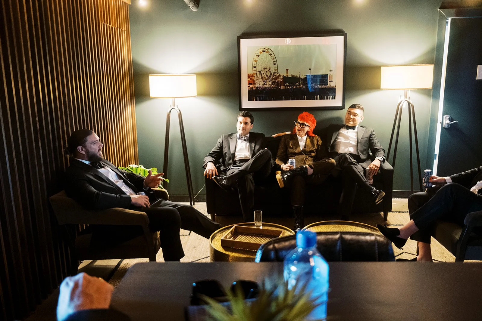 Groomsmen in tuxedos relax on the sofa beneath a Ferris wheel print in the Green Room