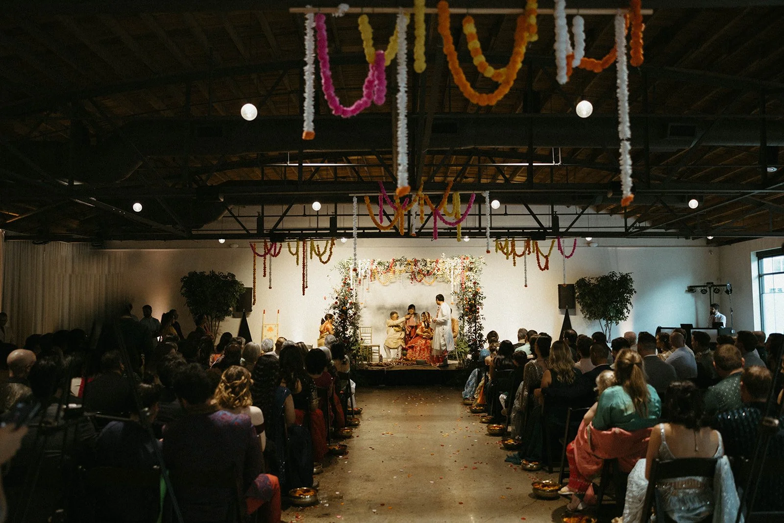 Wedding ceremony with colorful marigold garlands hanging from the truss ceiling and a floral mandap at the front