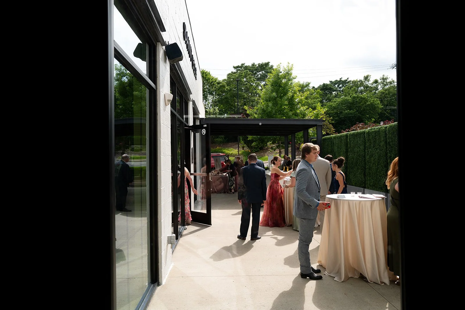 Cocktail hour on the patio seen through an open doorway, with guests at linen-draped highboys