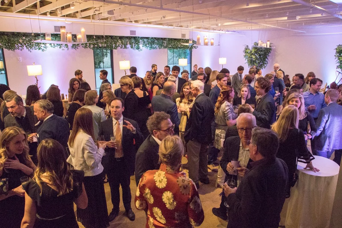 Guests mingle during cocktail hour in the Conservatory under a greenery garland and soft purple uplighting