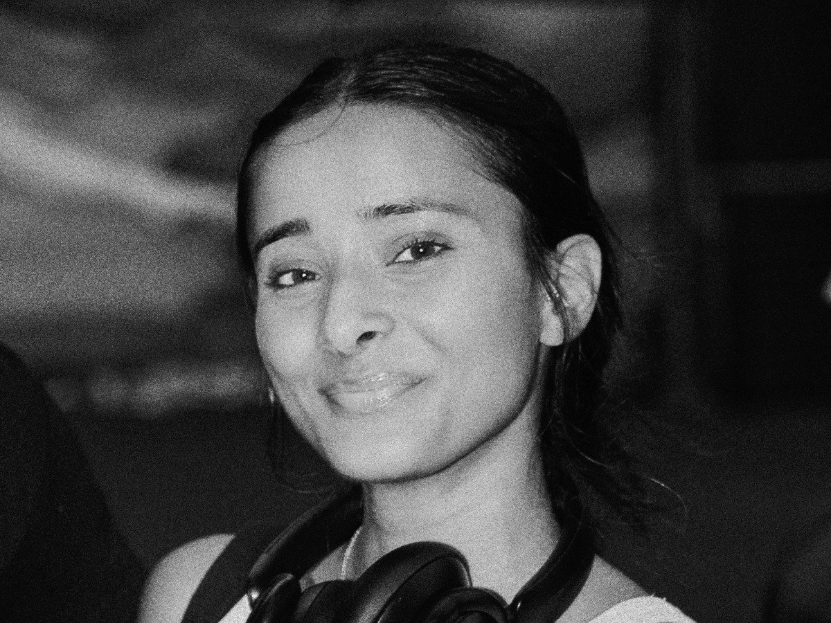 A black and white portrait of a woman with braided hair, looking over her shoulder, with a neutral expression waiting for a pickleball game. 