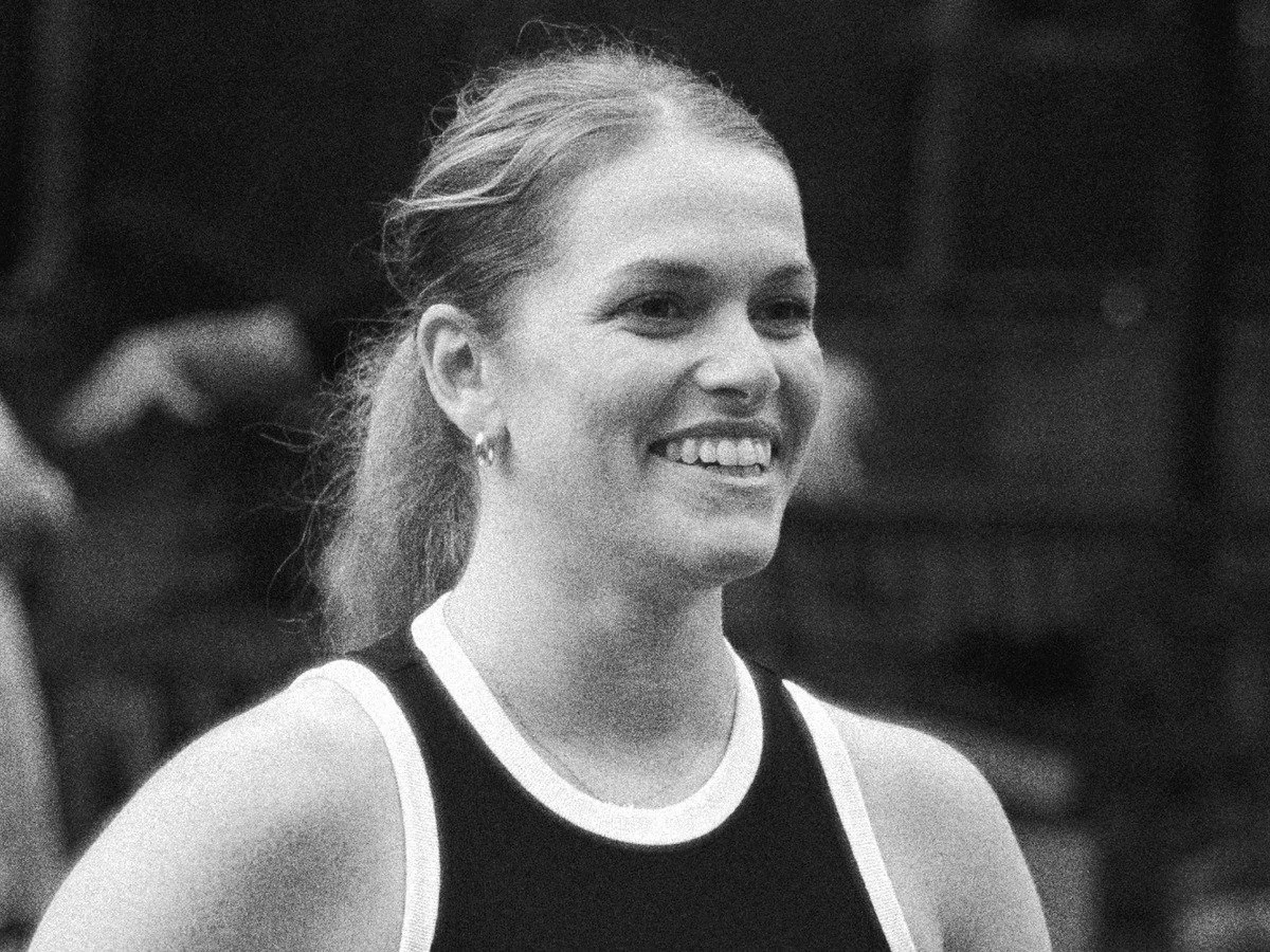 Black and white photo of a woman with long wavy hair, lying down with her hand on her face, looking at the camera waiting for a pickleball.