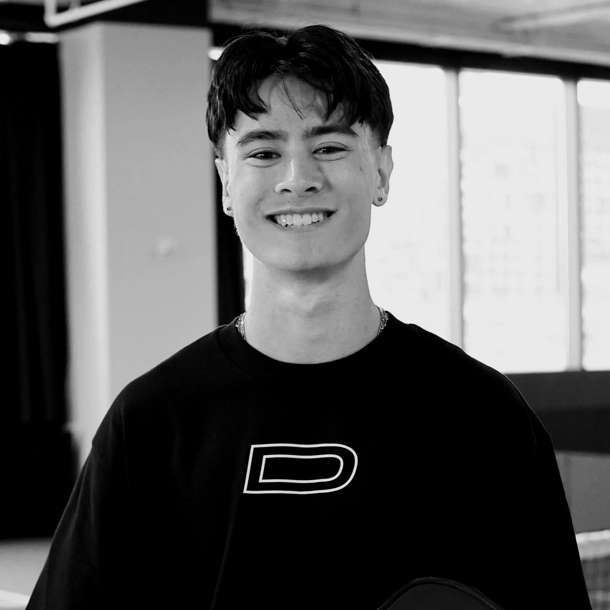 Black and white portrait of a young man with short hair, a goatee, wearing a white shirt, looking pensively into the distance coming from a pickleball game in NYC.