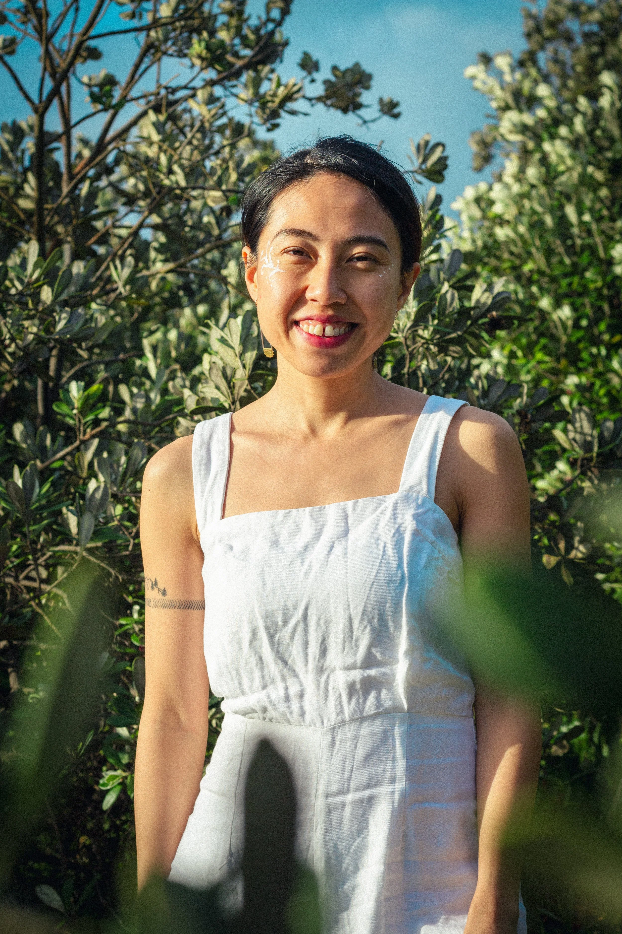 Woman in white dress standing outdoors among trees, smiling