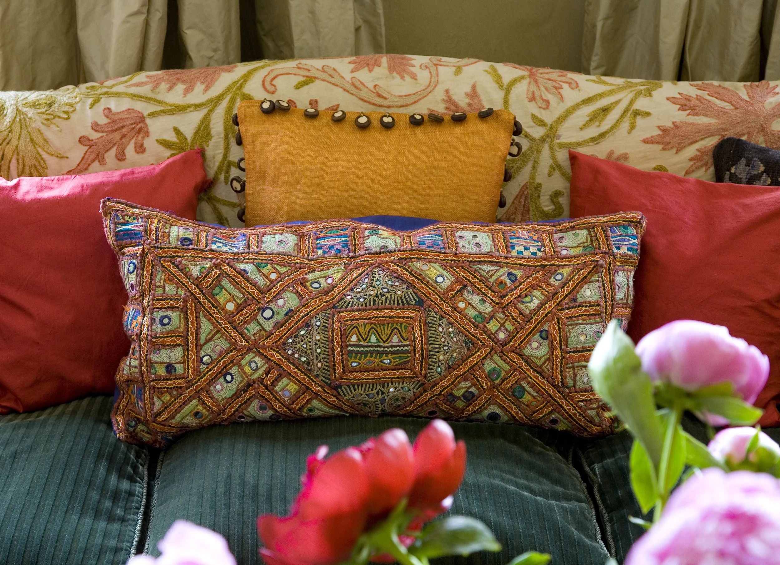 Array of colorful decorative pillows arranged on a sofa, with pink and yellow flowers in the foreground.