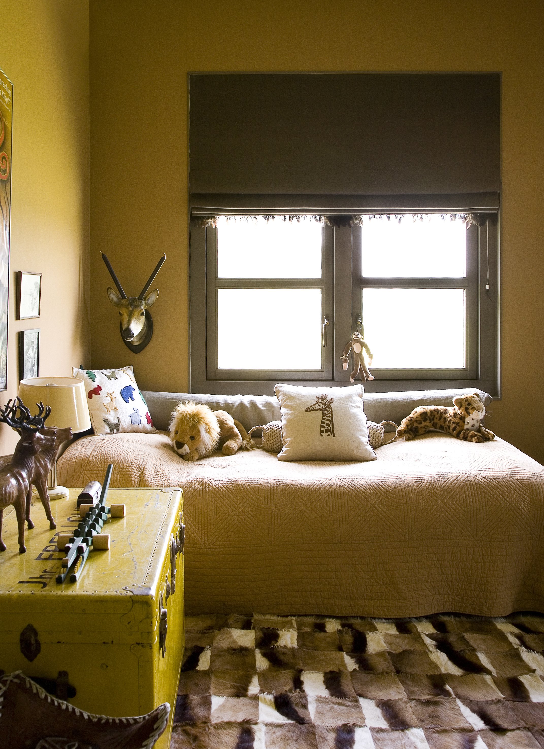 Cozy bedroom with a large window, plush bed, stuffed animal toys, animal-themed decorations on the wall, and a patterned rug.