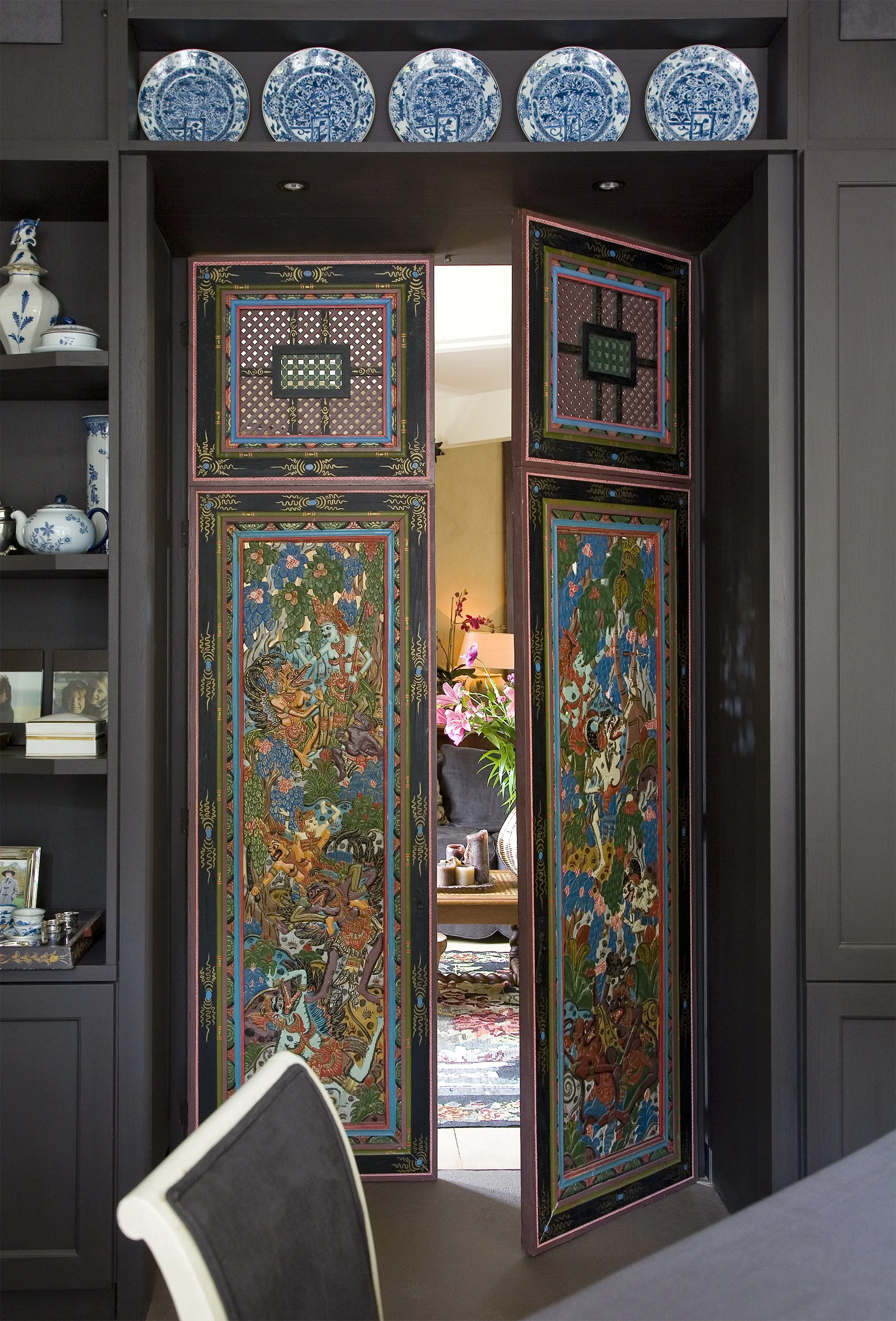 Decorative room divider with colorful Asian artwork partially open, revealing a living room with a plant and a lamp.