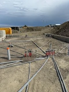 Construction site with electrical conduit pipes installed on a dirt ground, overcast sky