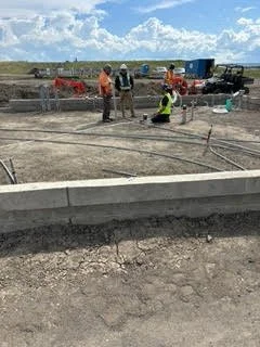 Construction workers on a building site, working with concrete and construction equipment under a partly cloudy sky.