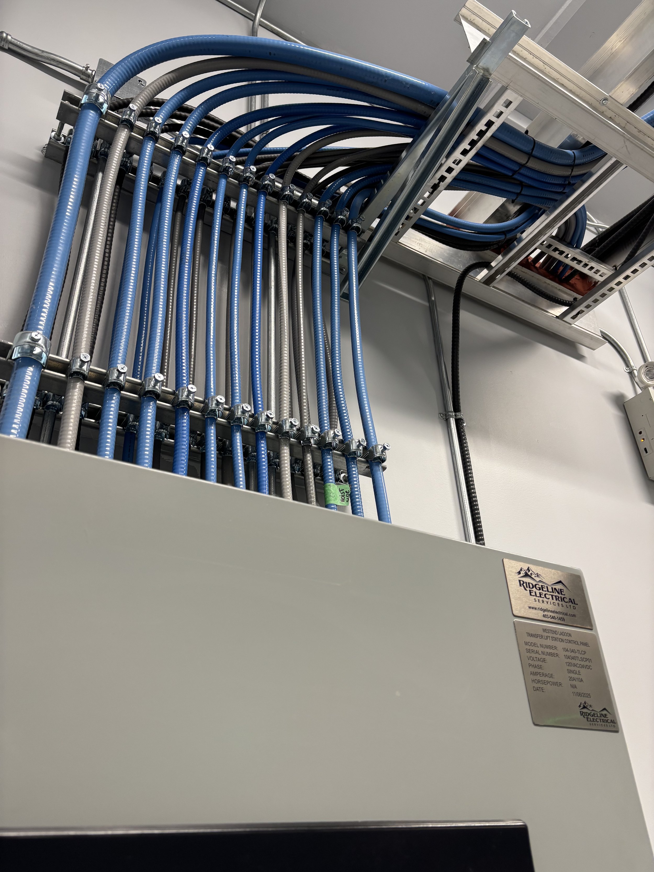 Electrical control panel with multiple blue and gray cables organized and connected to a metal structure, labeled with 'RidgeLine Electrical Services Ltd.'