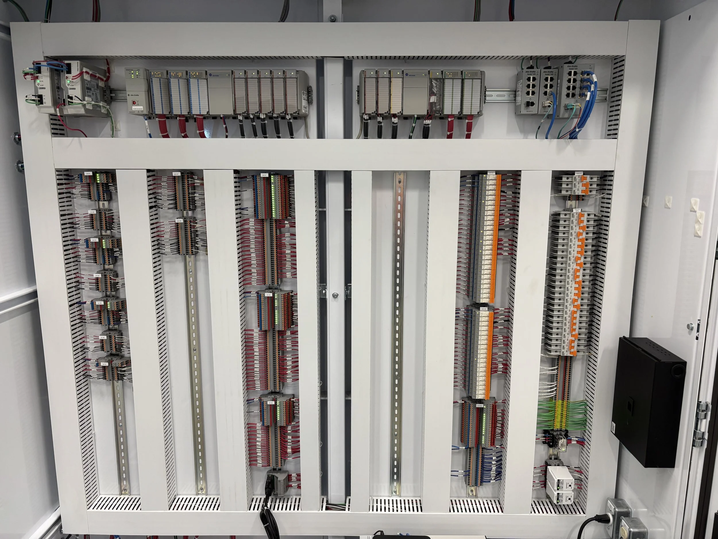 An electrical control panel with multiple wiring connections, circuit breakers, and wired modules arranged inside a metal enclosure.