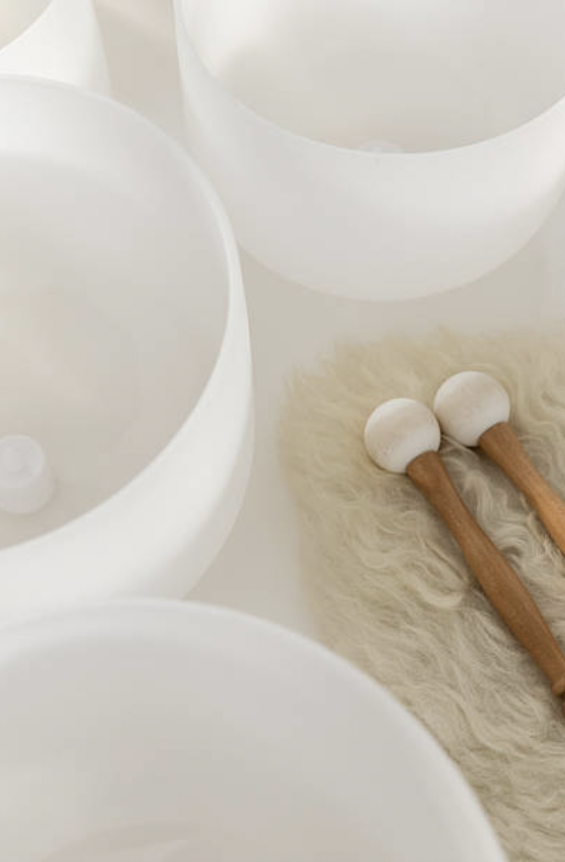 Three white bowls and two wooden mallets with white balls placed on a fluffy beige rug.