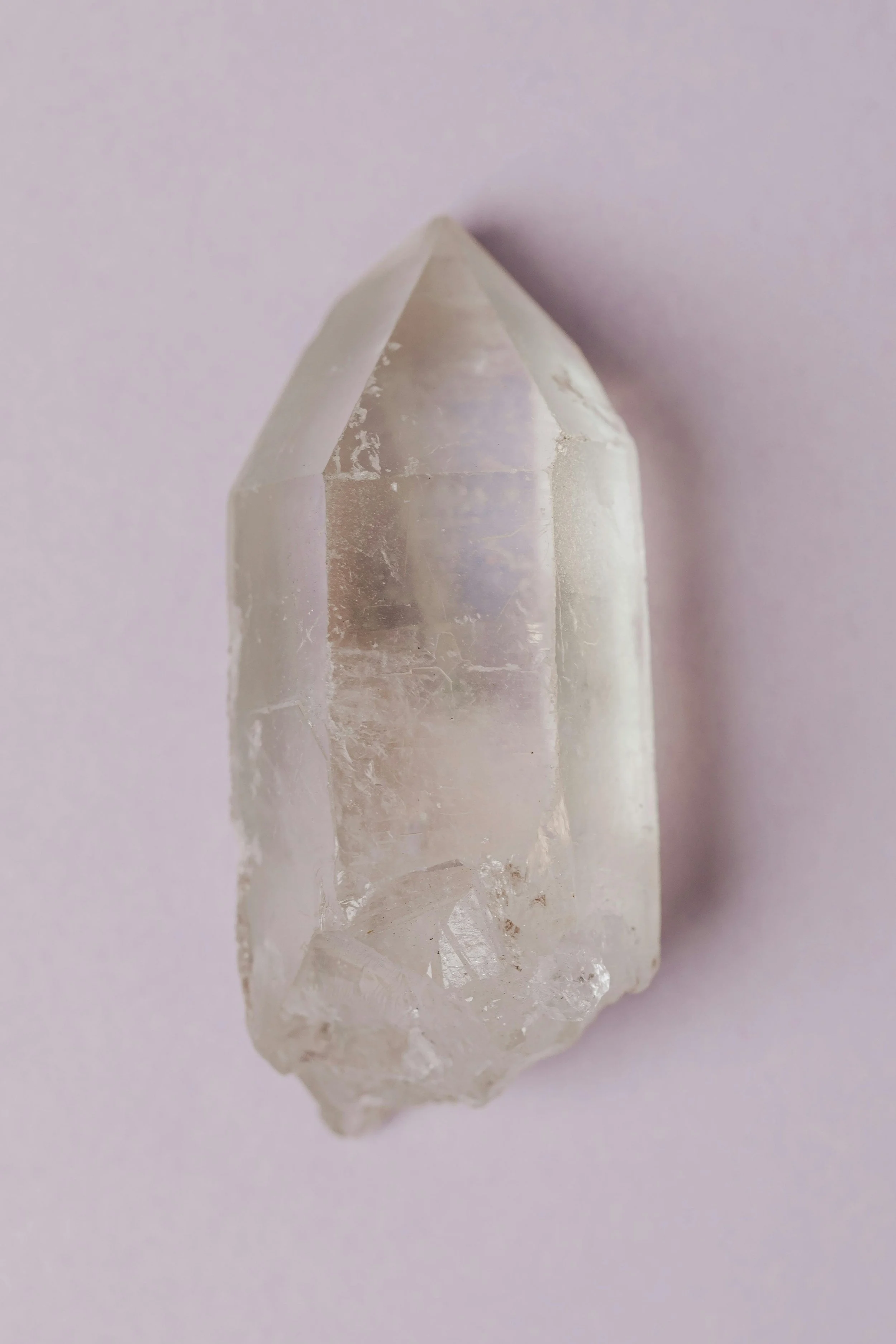 Close-up of a clear quartz crystal with a pointed tip on a light pink background.