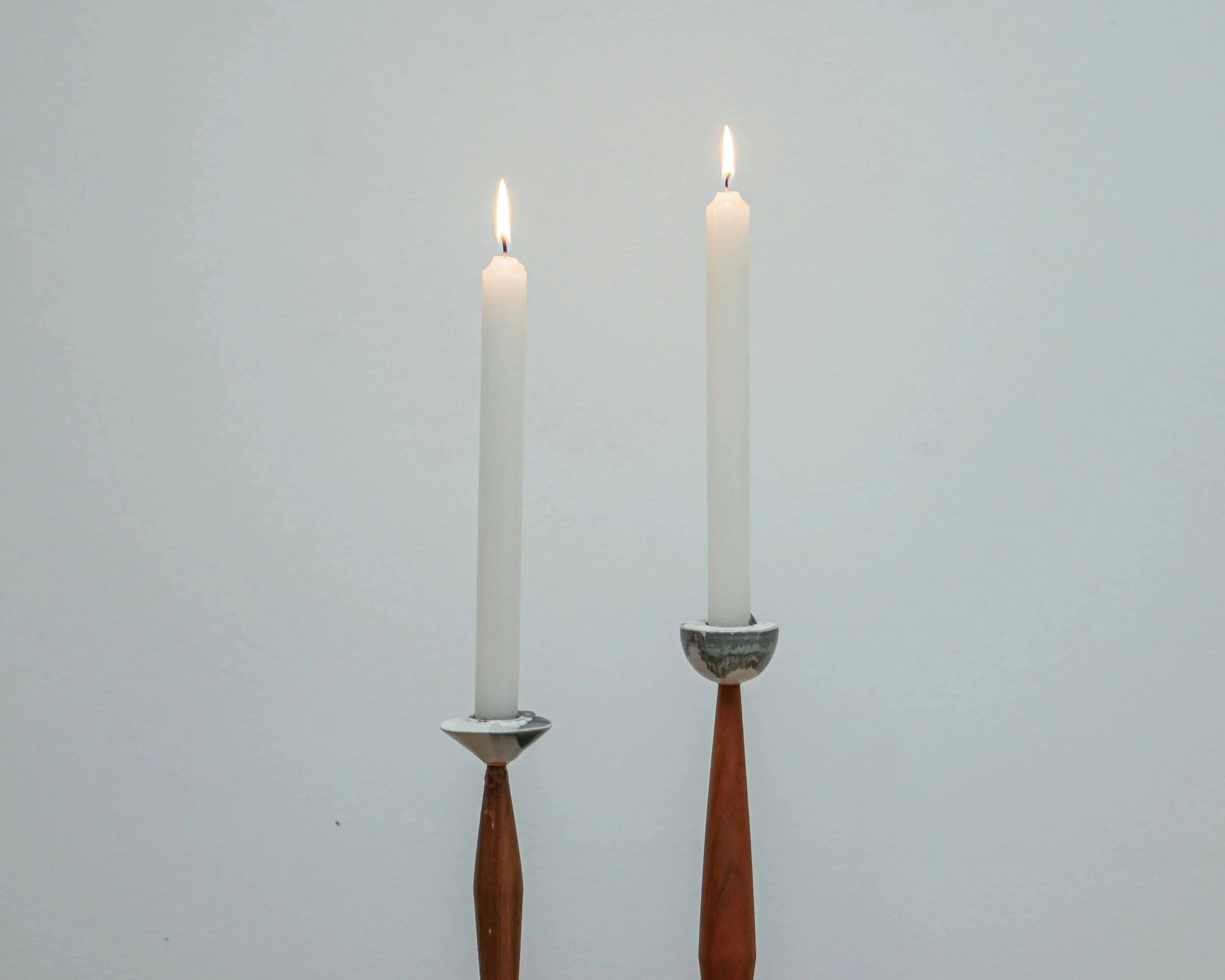 Three candles with wooden holders, unlit, in front of a plain light background.