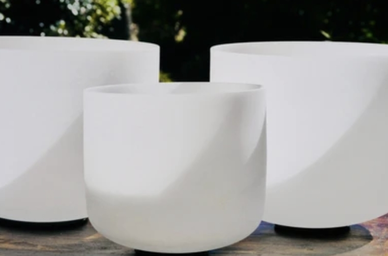 Three white ceramic vases with rounded shapes on a wooden surface outdoors, with greenery in the background.
