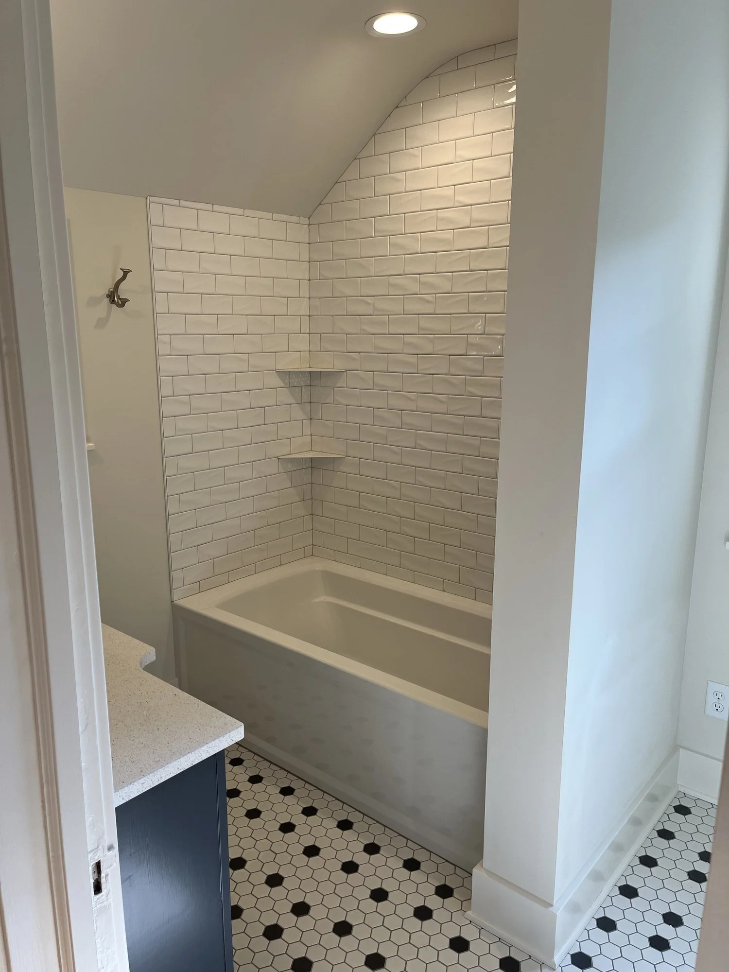 Bathroom with white subway tile shower, bathtub, black and white hexagon tile floor, blue vanity, and recessed lighting.