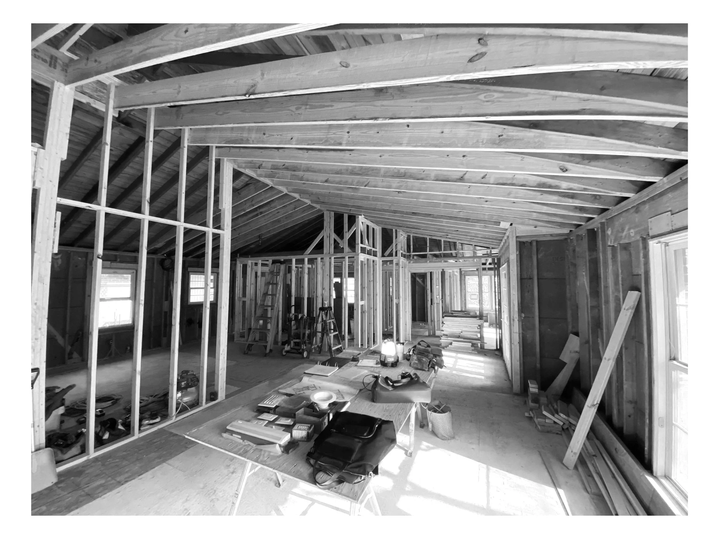 Interior view of a house under construction with visible wooden framing, tools, and building materials.