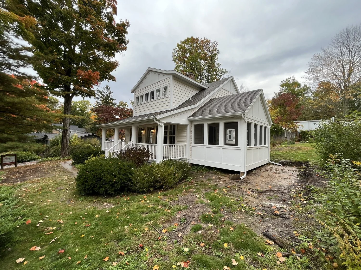 White two-story house with a porch surrounded by autumn trees and greenery.