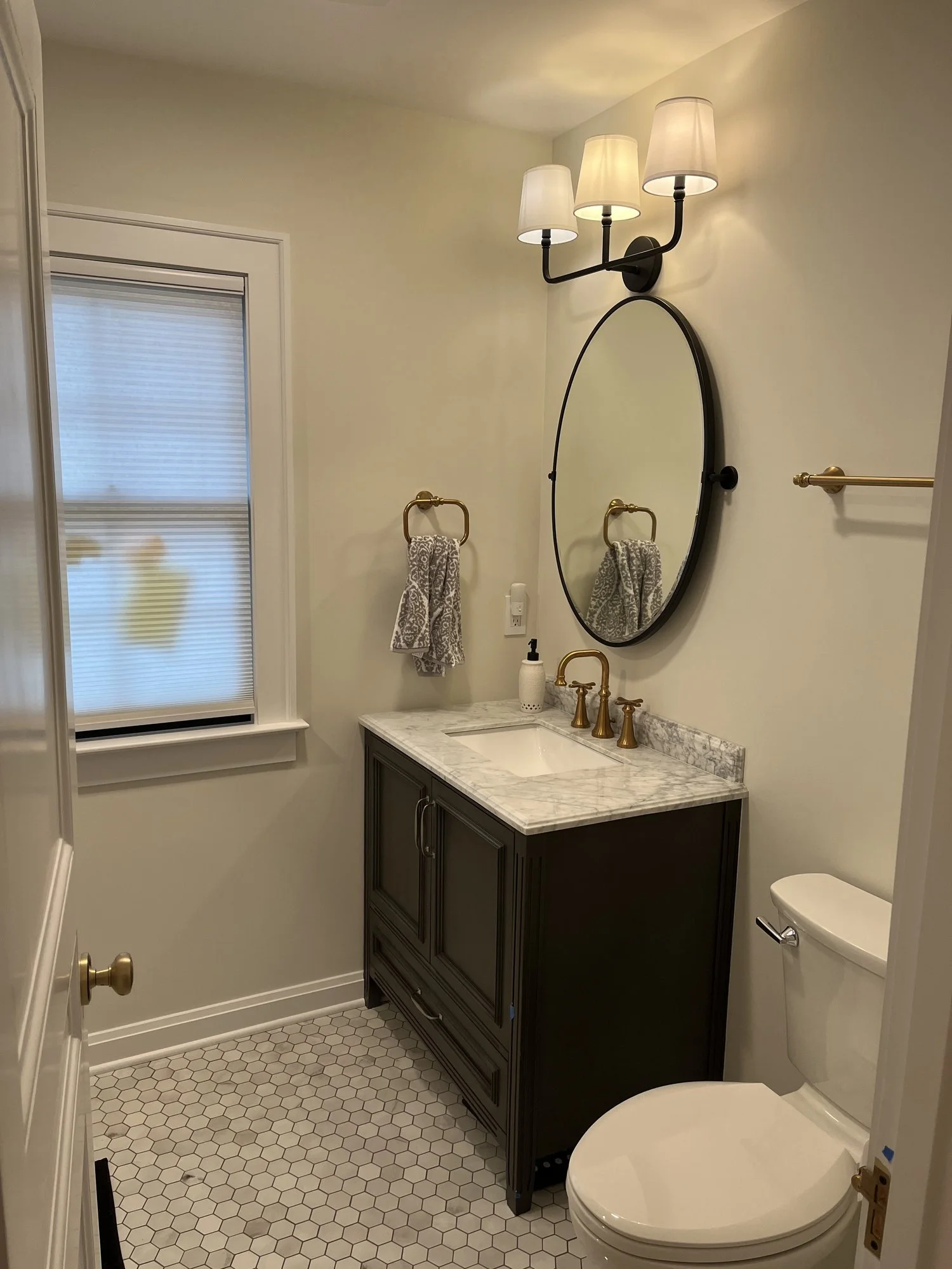 Modern bathroom with hexagonal tile flooring, a vanity with a marble countertop, round mirror, and three light wall fixture.