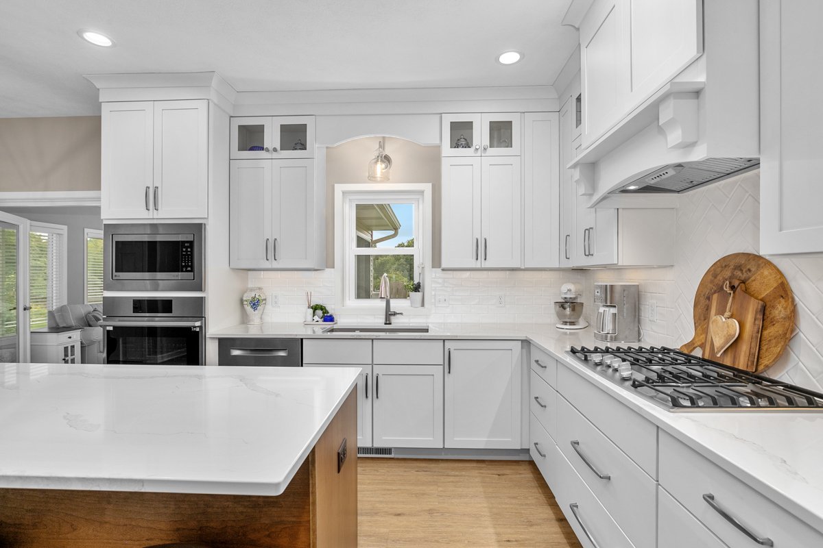 Modern white kitchen with island, stainless steel appliances, and wooden cutting board on the counter.