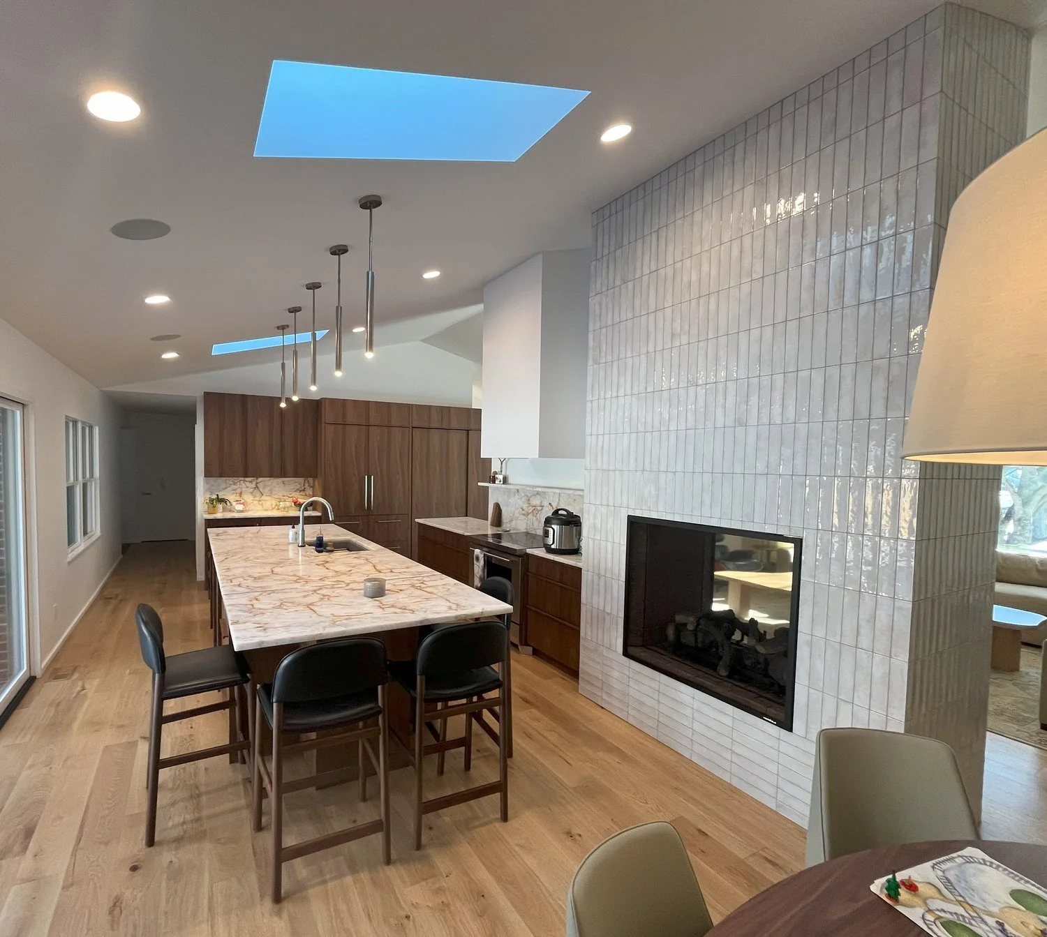 Modern kitchen with marble island, wood cabinetry, and tiled fireplace.