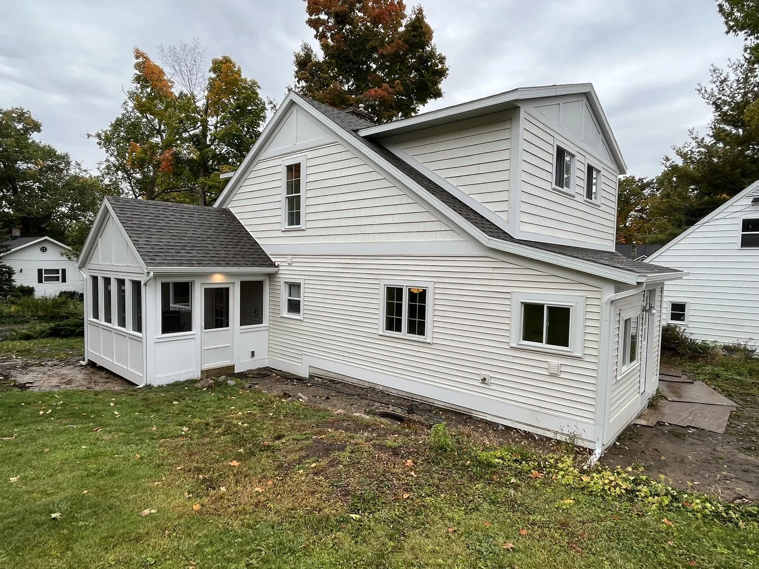 A white two-story house with a porch and grassy yard in autumn.