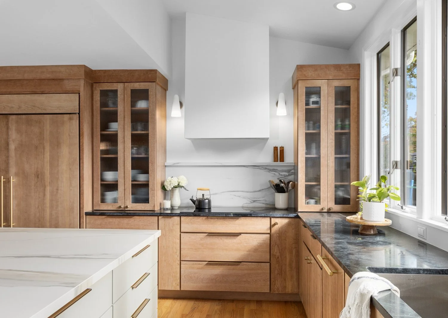 Modern kitchen with wooden cabinets, marble countertops, and stainless steel fixtures.