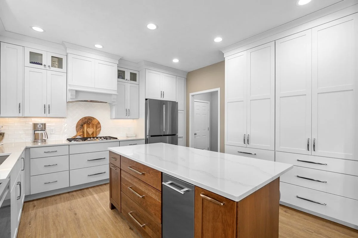 Modern kitchen with white cabinets, a large island, stainless steel refrigerator, and wood flooring.