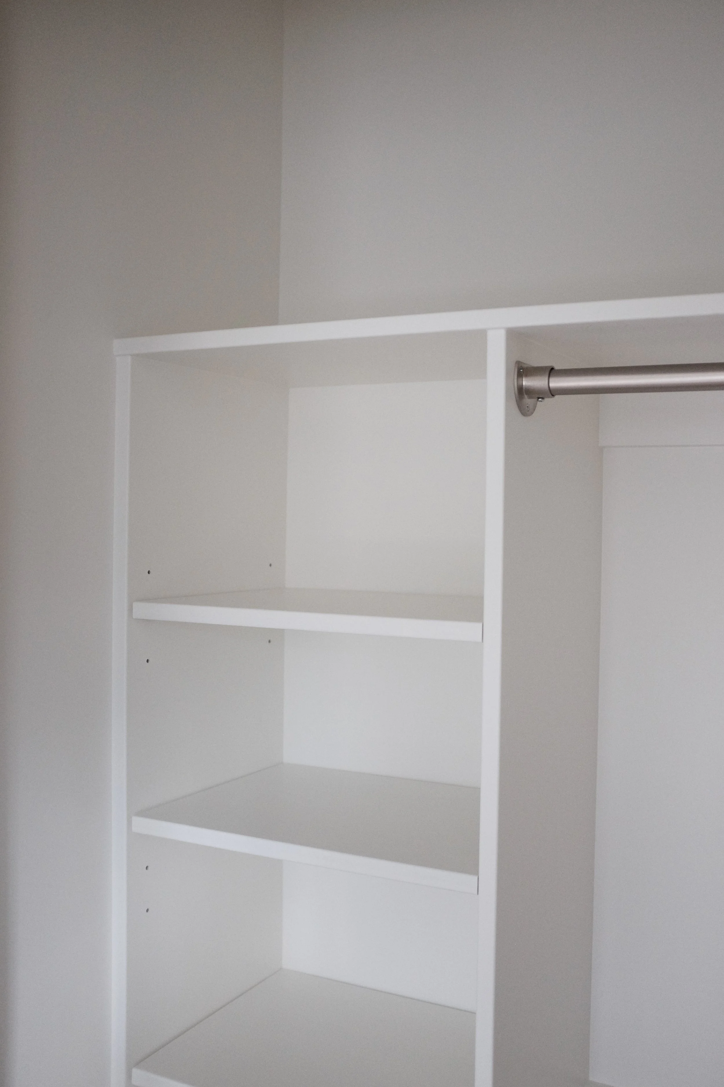 Empty white closet with shelves and a hanging rod.