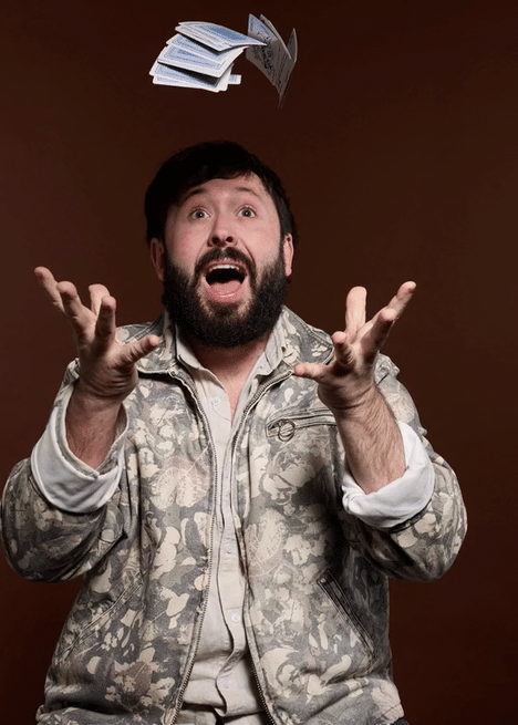 A man with a beard and dark hair throwing papers into the air, expressing surprise or excitement.