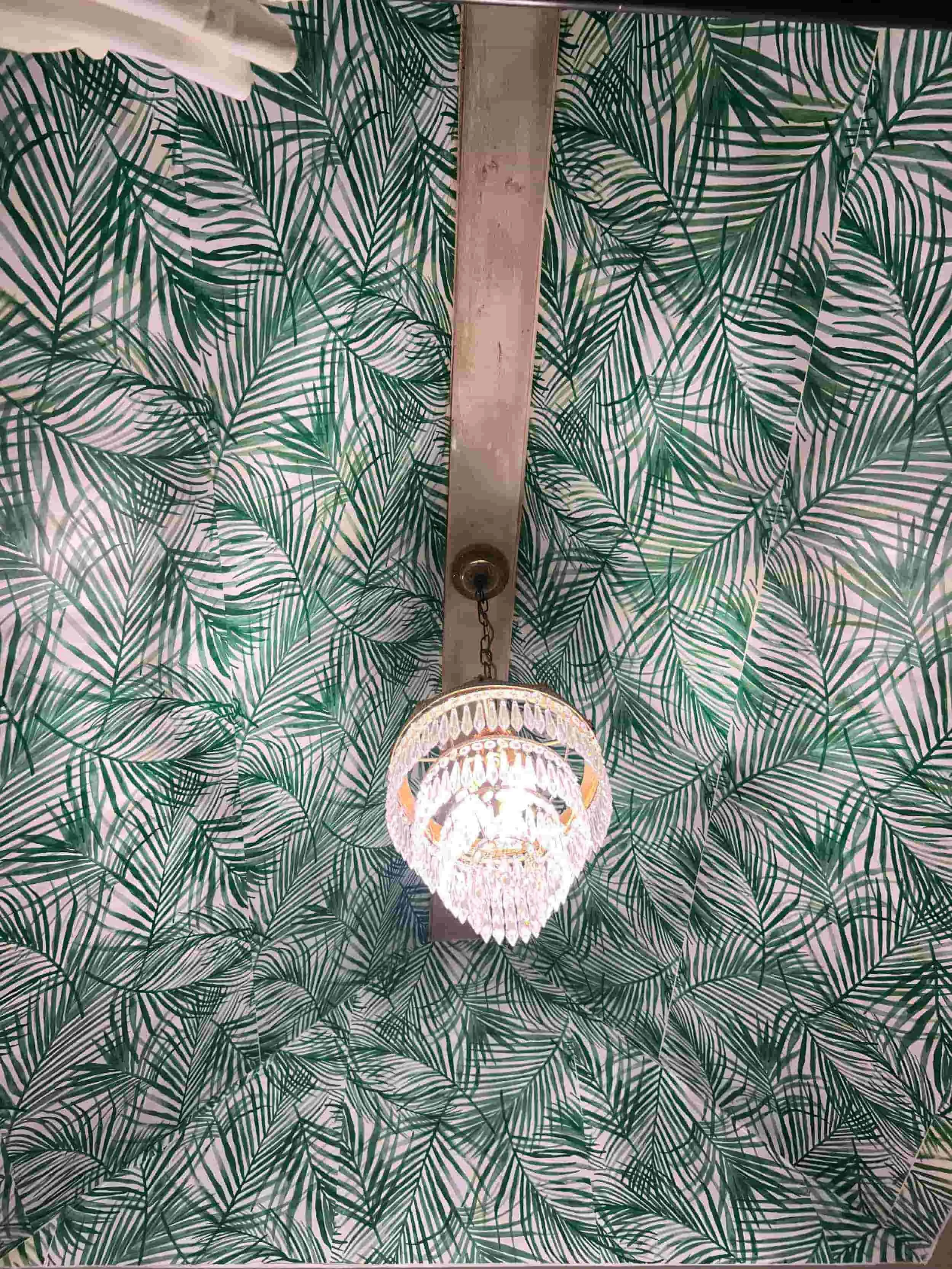 A ceiling with a tropical leaf patterned wallpaper and a hanging chandelier light fixture.