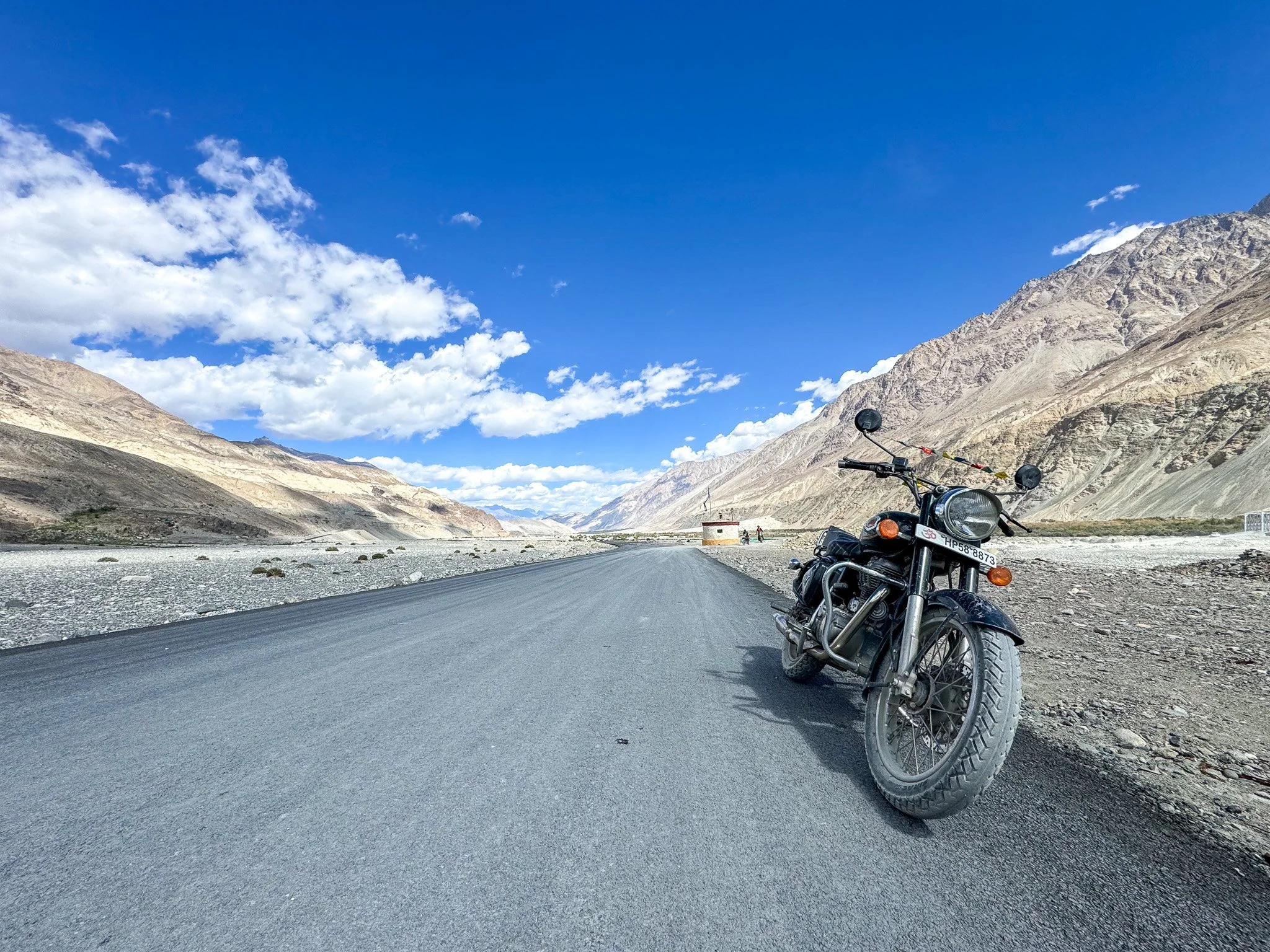 A motorcycle parked on the side of a mountain road with mountains and blue sky in the background.