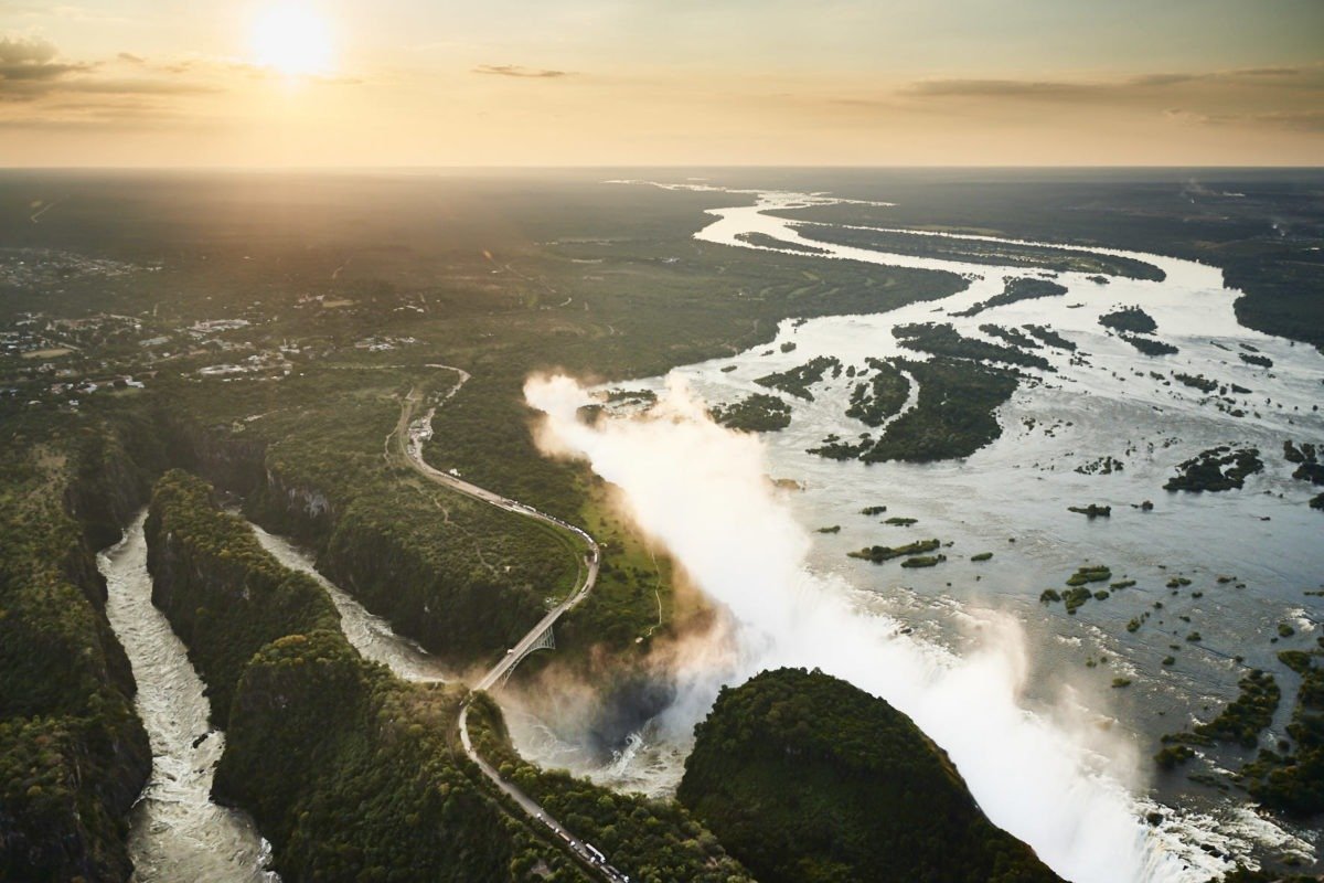 Aerial view of Niagara Falls during sunset, showing waterfalls, cliffs, and a river, with mist rising from the falls.