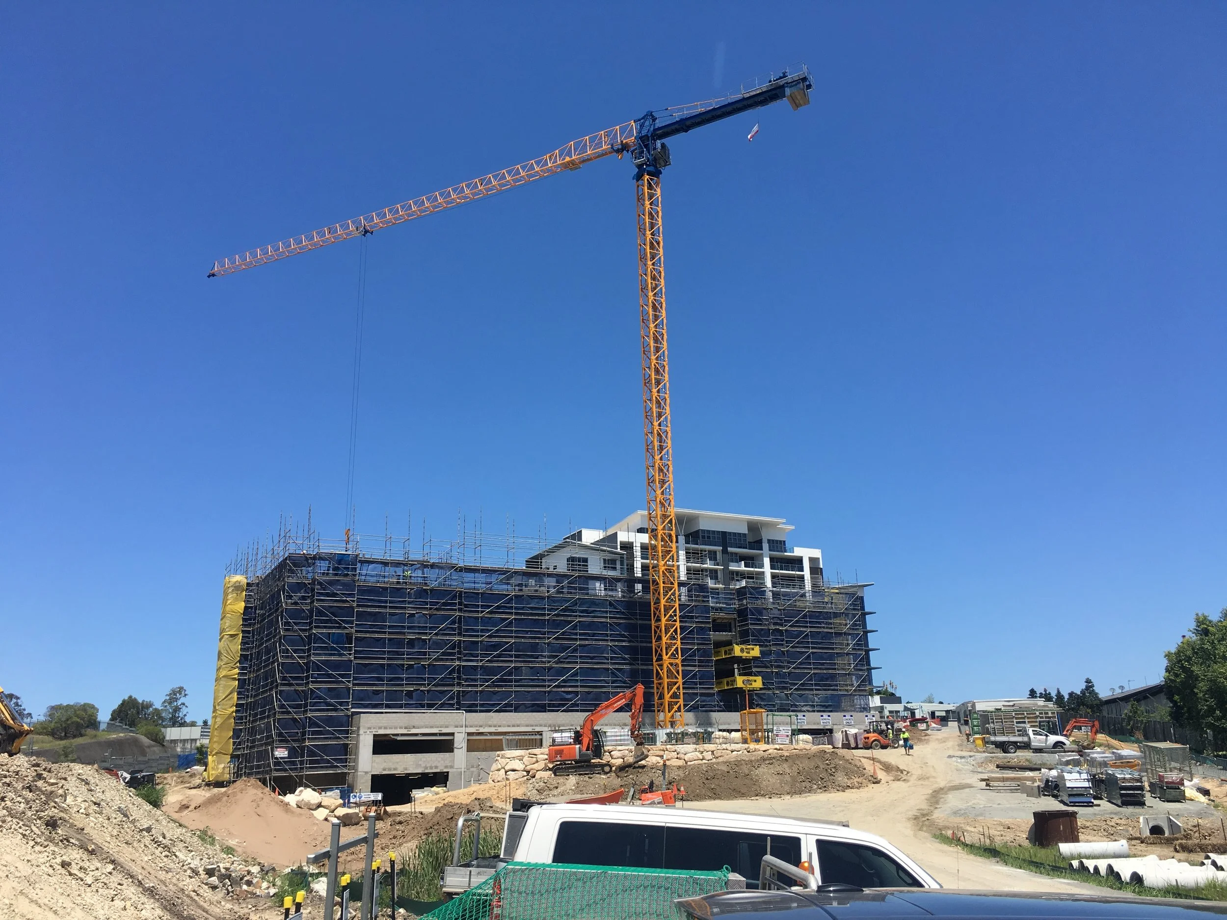 Construction site with a tall crane, building scaffolding, and vehicles under clear blue sky.