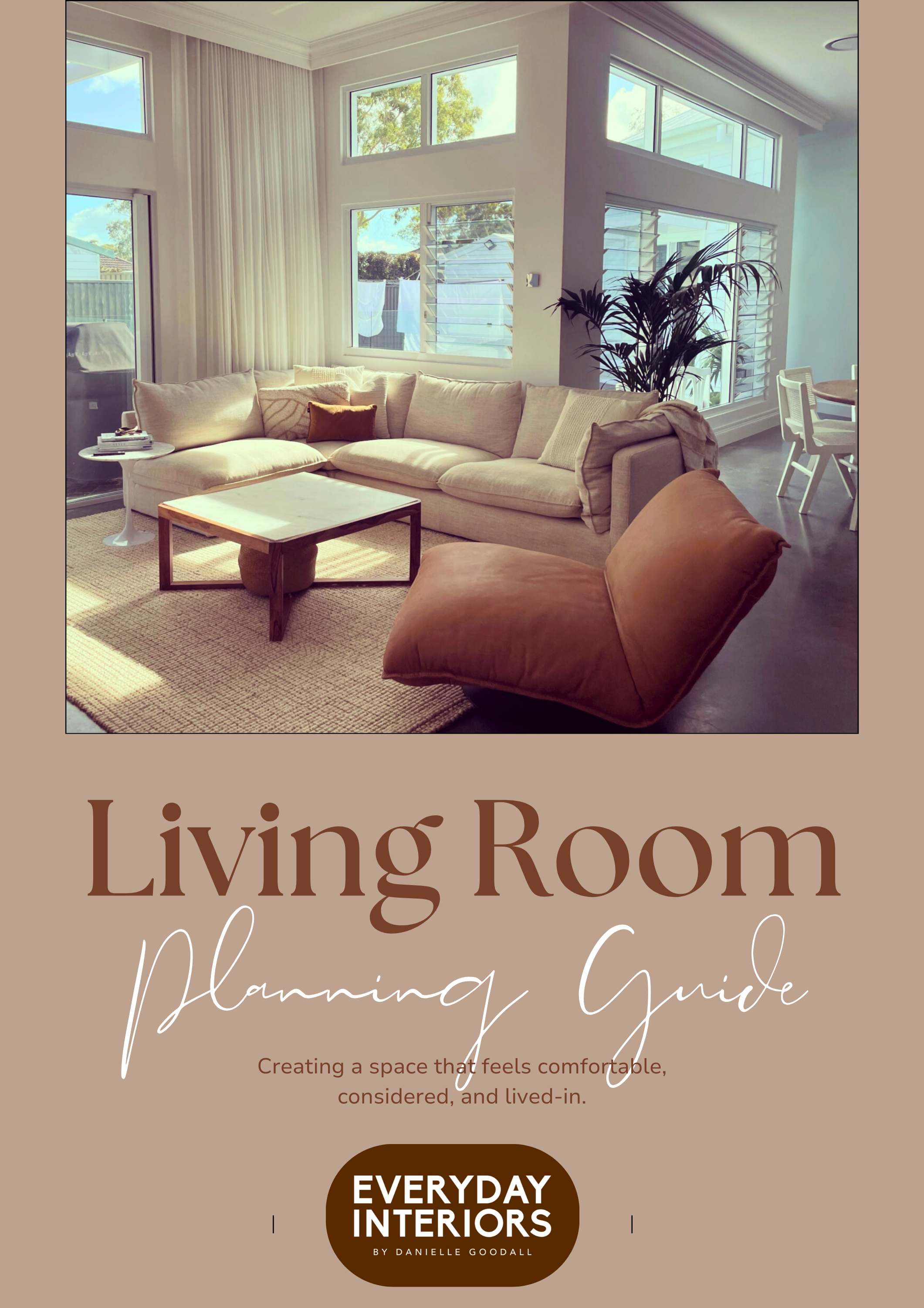 A living room with a beige sectional sofa, a brown leather chair, a white coffee table, and large windows with blinds and curtains, overlooking trees and neighboring houses.