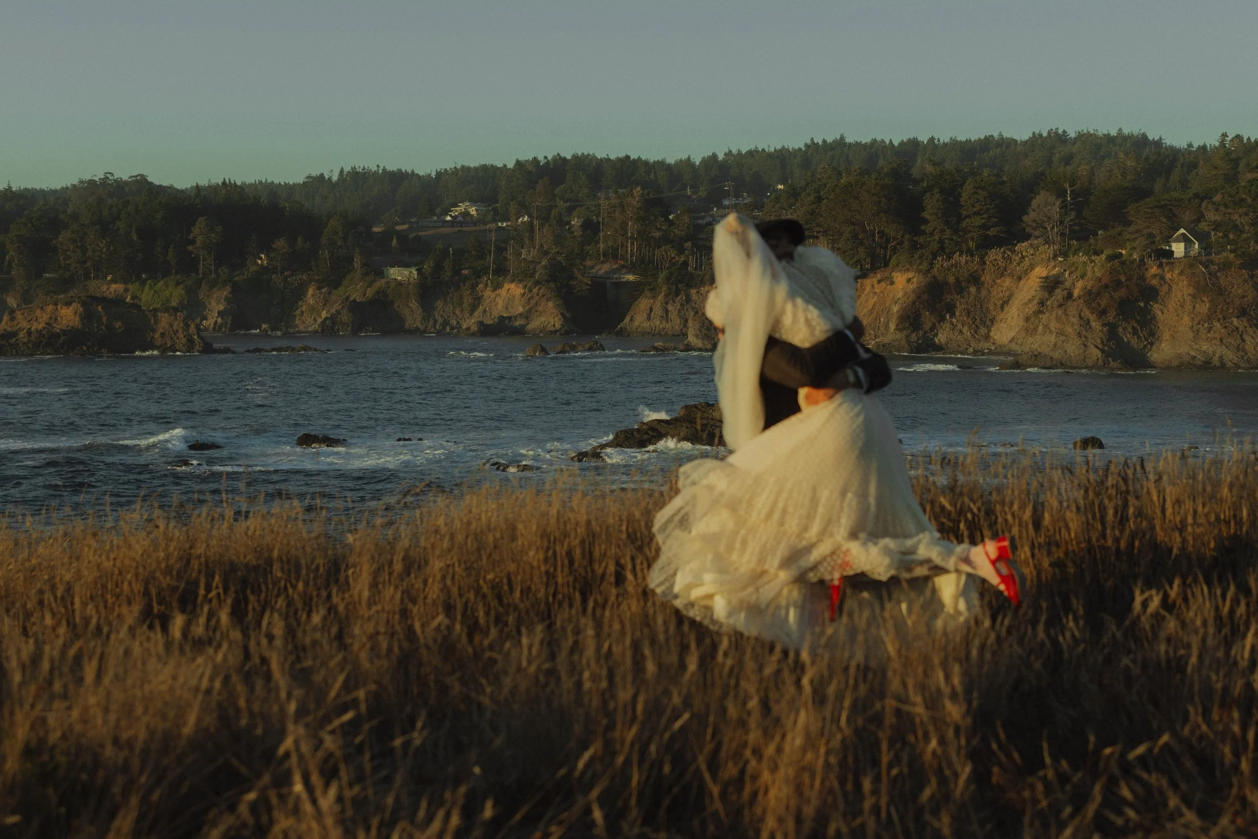 Bride and groom laughing and running along the Northern California coastline during a cinematic wedding session by San Francisco photographer Kirstin Mullins.