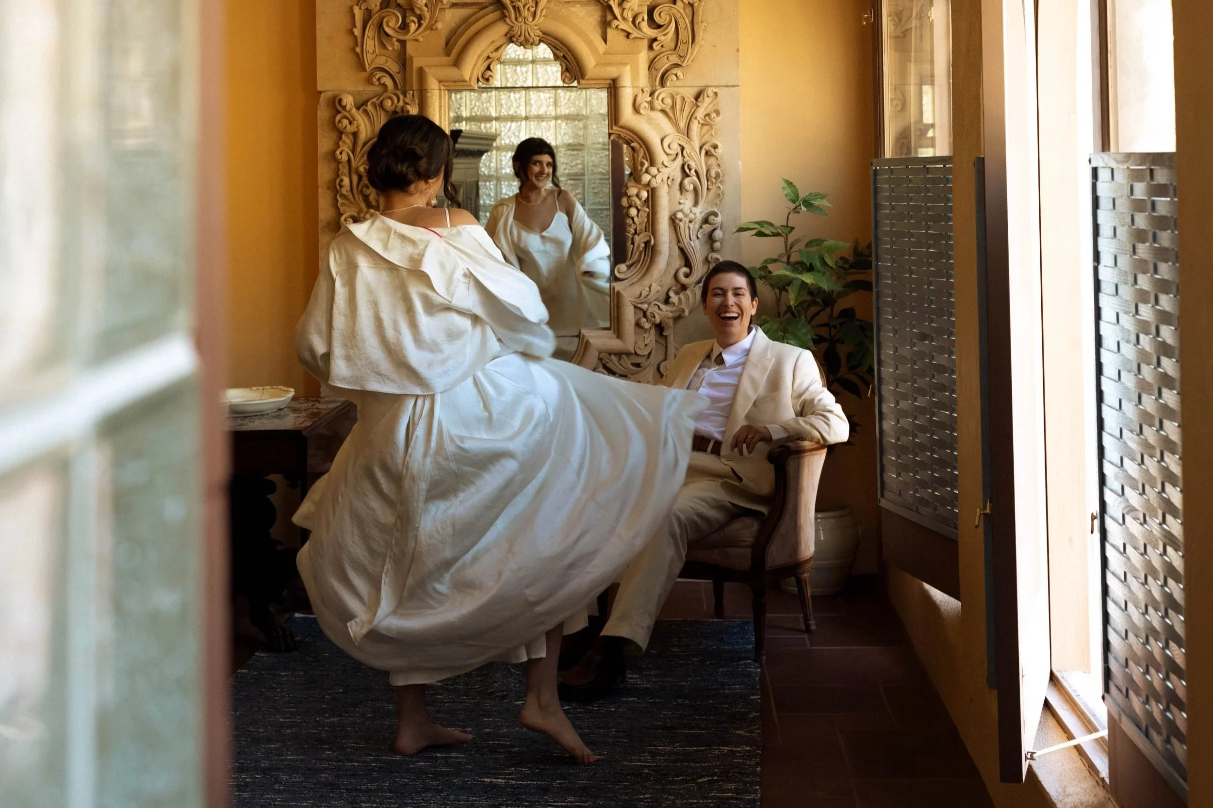 Candid moment of a bride twirling her dress while her wife laughs during a San Francisco wedding morning.