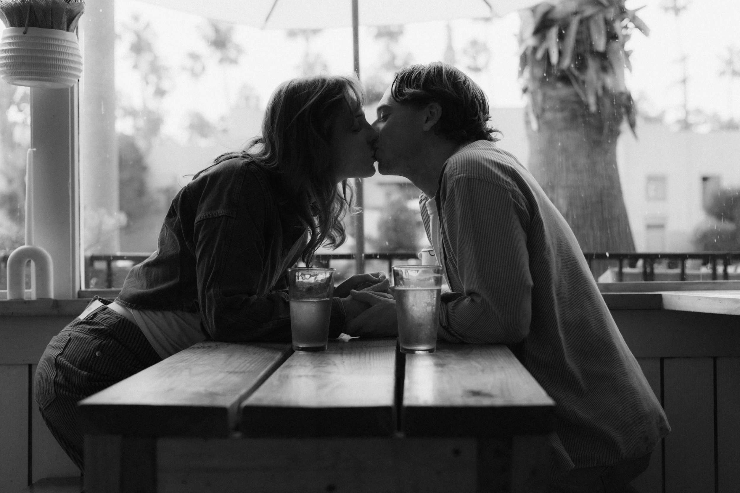 Candid couples photo of two partners kissing across a café table during a date-night session in San Francisco.