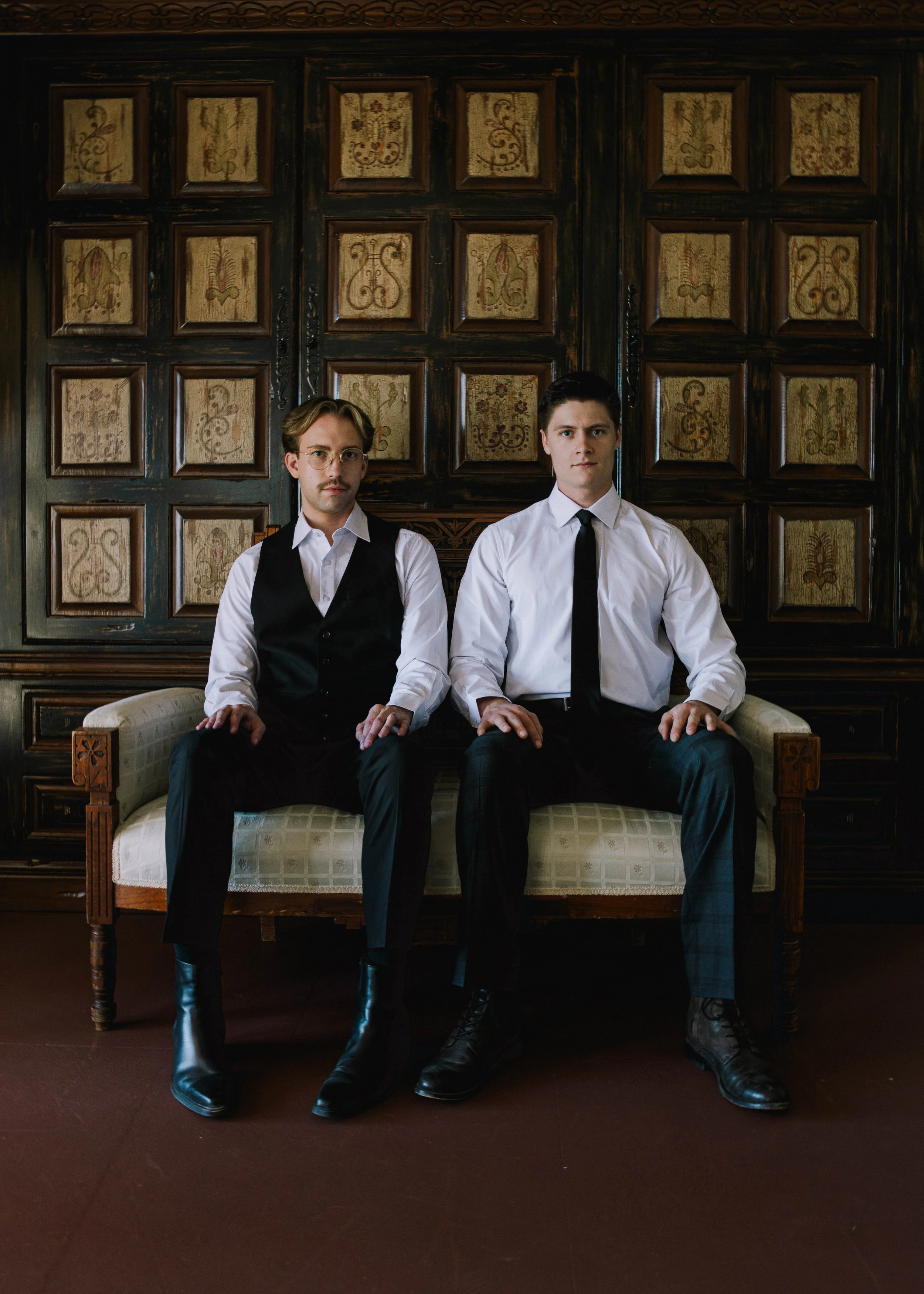 Editorial wedding portrait of two grooms sitting formally on a vintage couch during their San Francisco celebration.