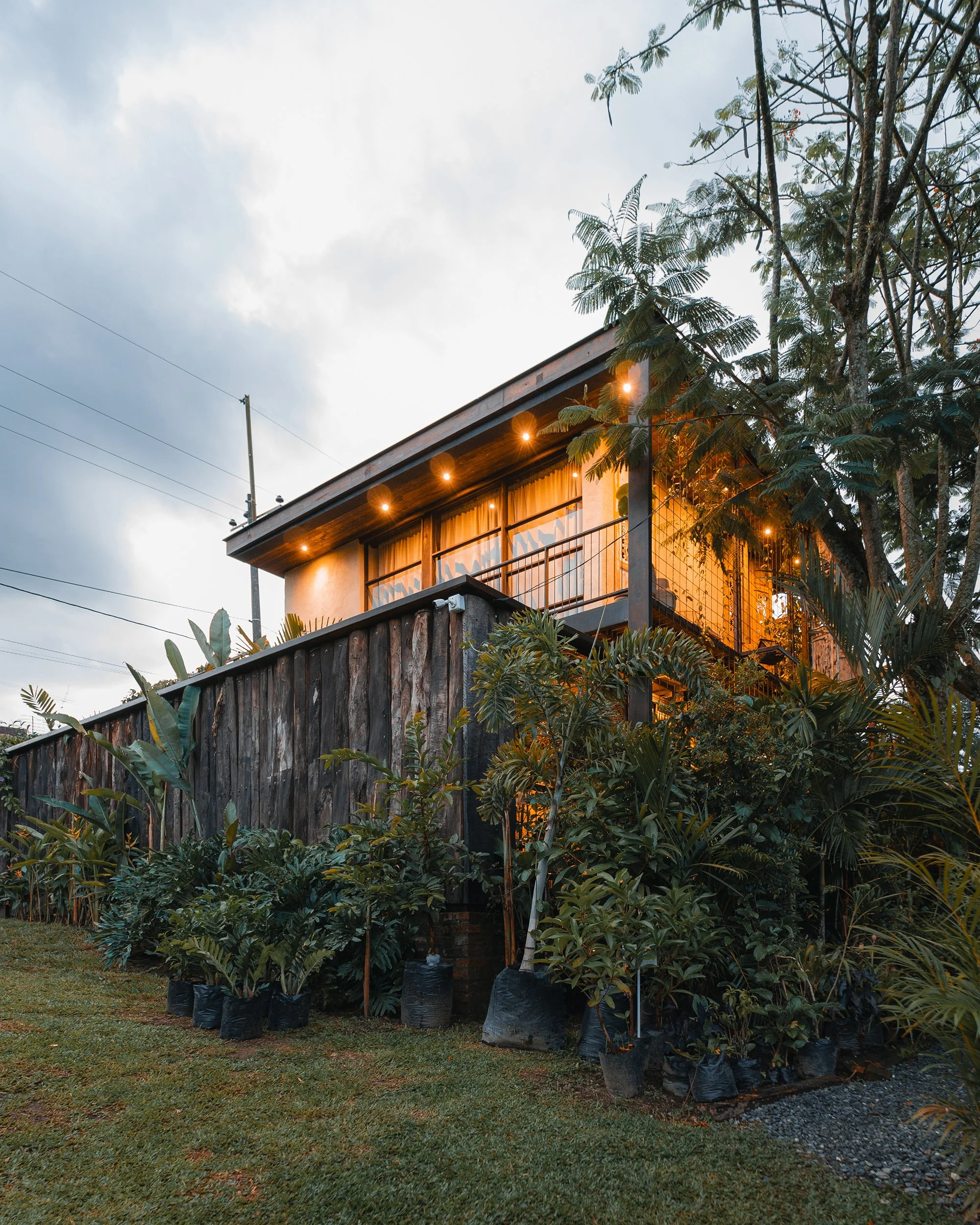 Fotografía de arquitectura residencial de una casa de dos niveles, con cerramiento en madera y rodeada de abundante vegetación