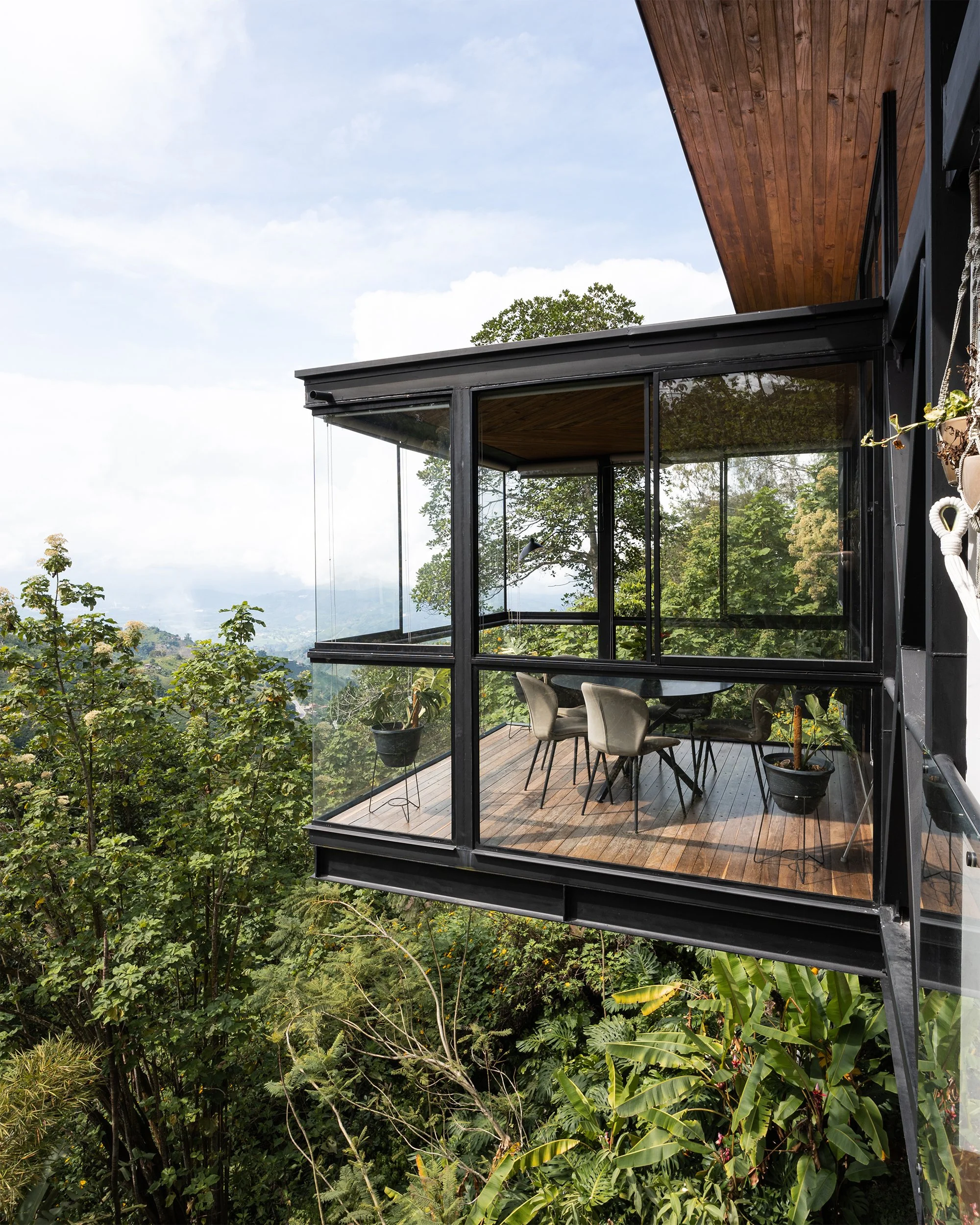 Fotografía de arquitectura residencial. Caja de vidrio en voladizo, comedor flotando sobre el paisaje y mucha vegetación