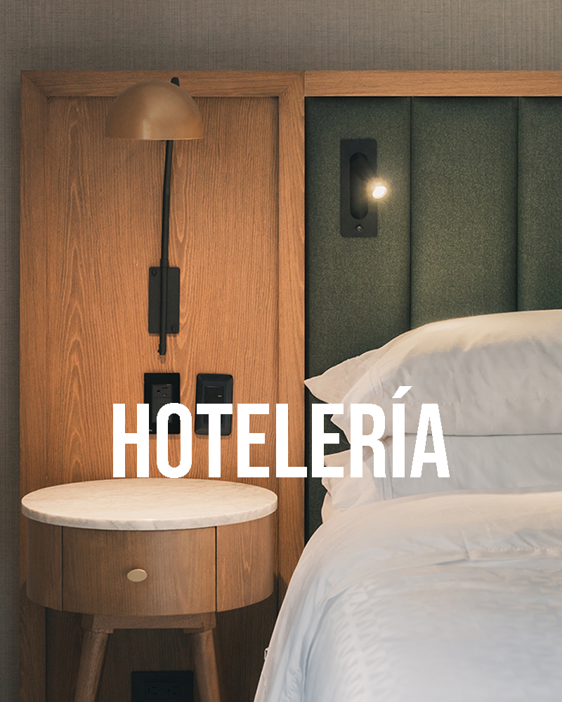 Fotografía hotelera del cabecero de una cama en madera, con una mesa de noche en madera, una iluminación moderna y sabanas blancas