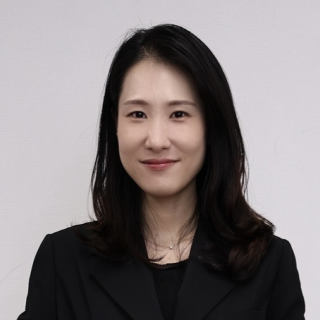 Portrait of a woman with shoulder-length black hair, smiling, wearing a black blazer, against a plain white background.
