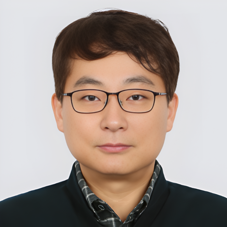 Portrait of a young man with glasses, wearing a dark blazer and patterned shirt, against a plain white background.