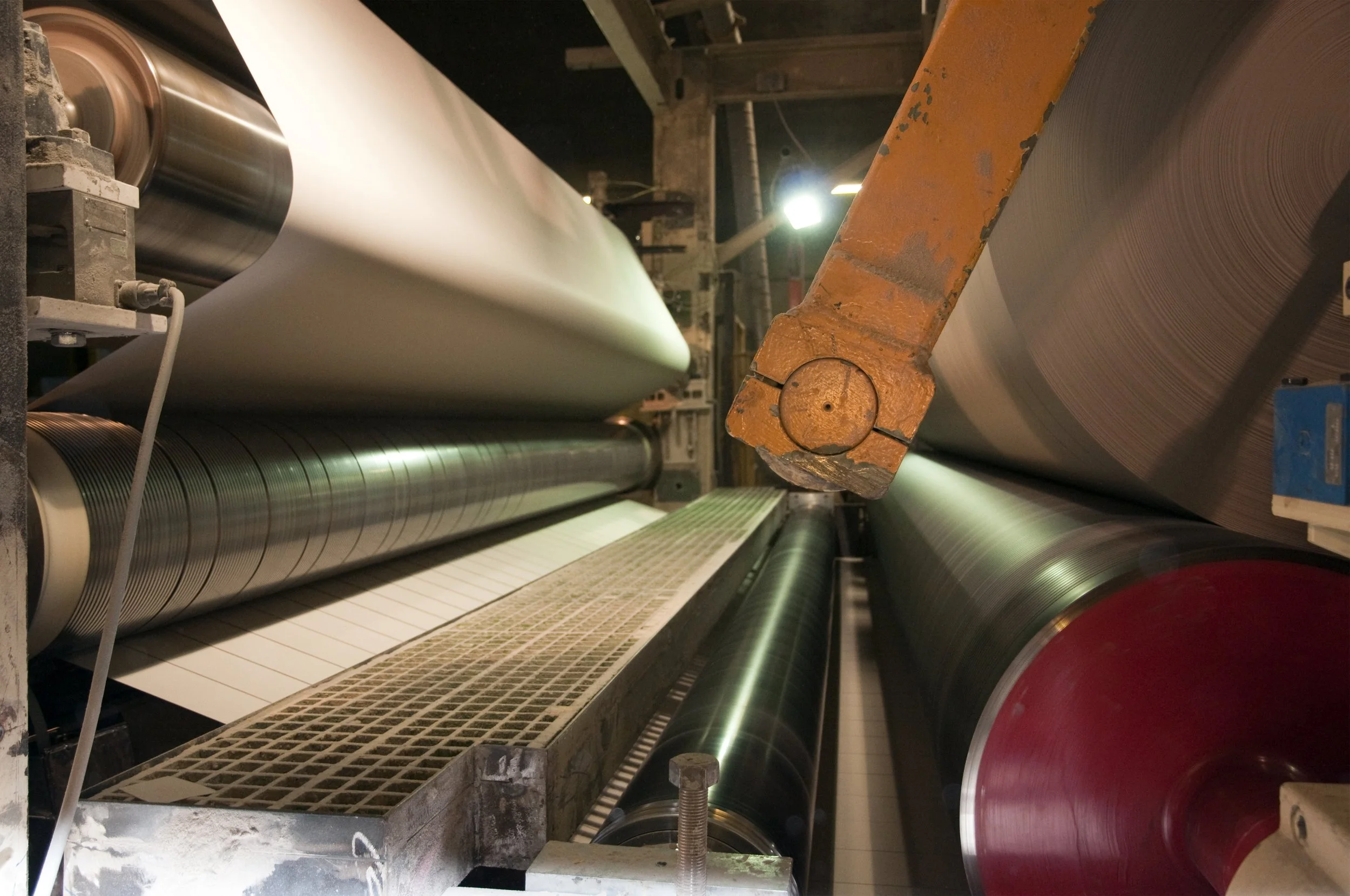 Industrial manufacturing machine with large metal rollers producing a wide sheet of material.