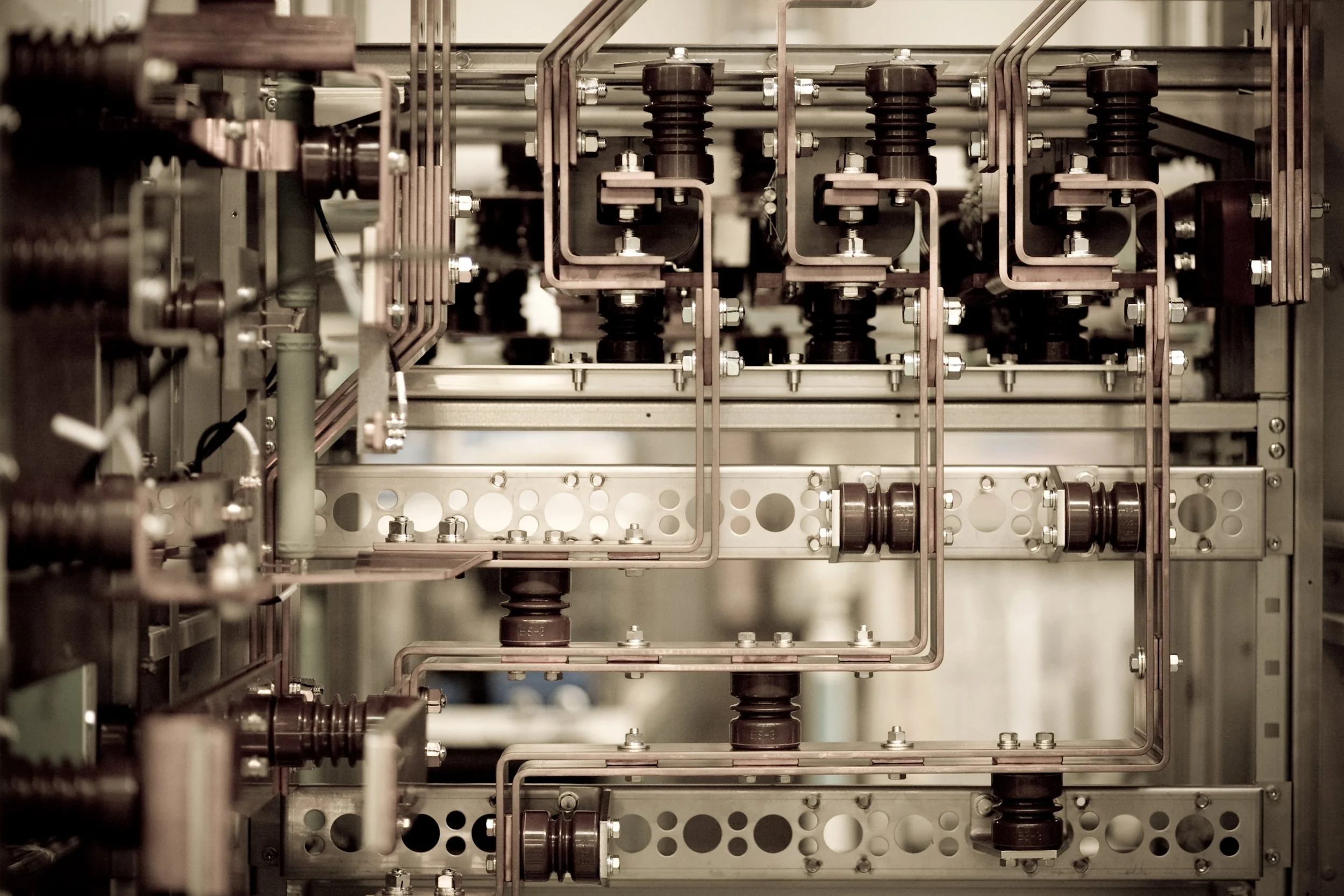 Close-up of an industrial machine with metal pipes, bolts, and black insulators, likely used in manufacturing or engineering.